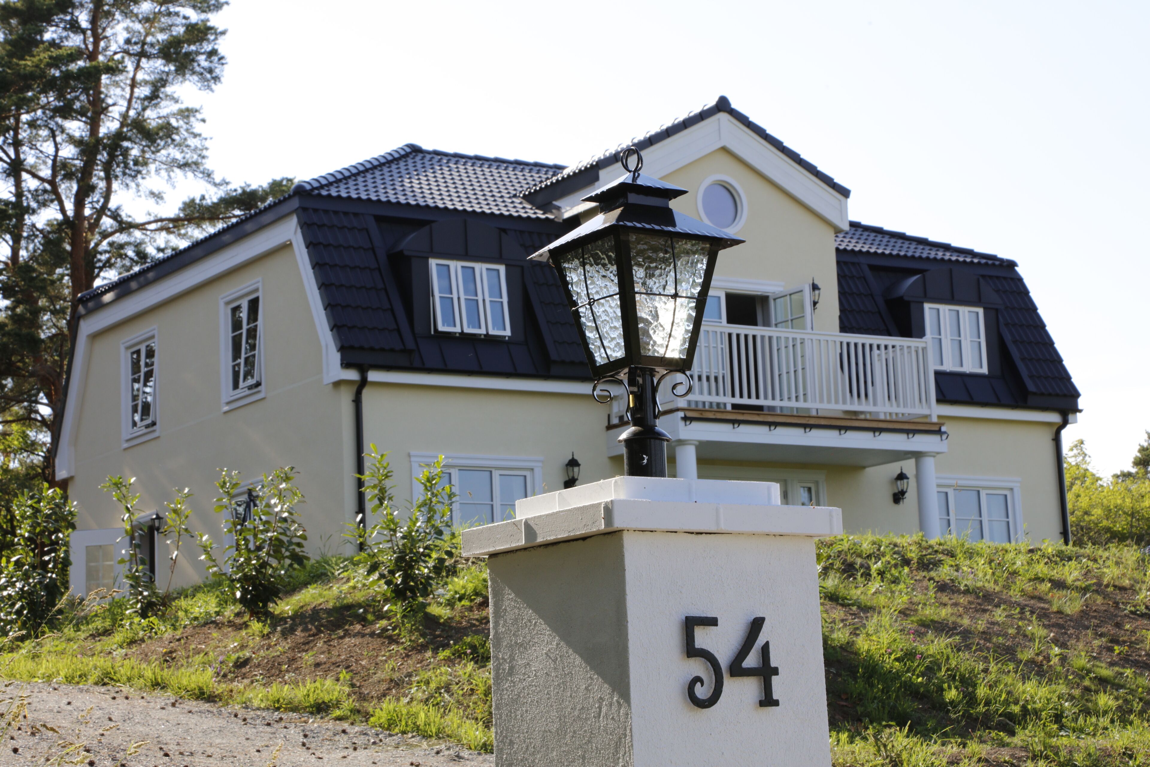 A two-story house with a balcony, a black roof, and a white fence.