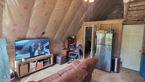 Ett litet, mysigt rum på vinden med en tv, en soffa, ett kylskåp och en dörr som leder till ett annat rum.