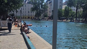 A riverside walkway with a brick pavement, a blue-painted railing, and people sitting by the water. - I'm renting out my apartment, located 15 meters from the Canal Saint-Martin in the 10th arrondissement. (Paris)