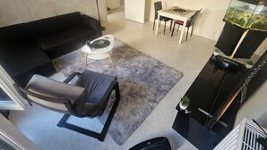 A living room with a black sofa, a grey armchair, a small white table, a fish tank, and a dining area with a table and chairs. - I'm renting out my apartment, located 15 meters from the Canal Saint-Martin in the 10th arrondissement. (Paris)