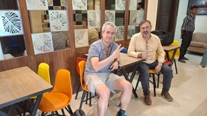 Un interior de restaurante con mesas de madera, sillas naranjas y motivos de hojas decorativas en las paredes.