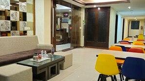 Un vestíbulo de hotel con una zona de estar, un mostrador de recepción y un área de comedor con sillas de colores.