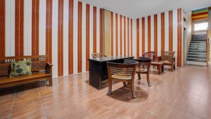 A room with striped wallpaper, a wooden bench, a desk with chairs, and a staircase. - Pelangi Guest House Cozy Stay (Curug)