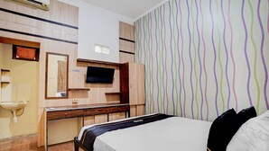 A hotel room with a bed, a desk with a flat-screen TV, a mirror, and a wall with striped wallpaper. - Pelangi Guest House Cozy Stay (Curug)