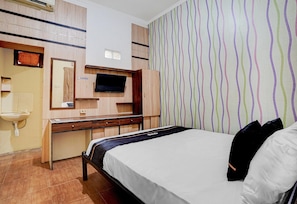 Habitación de hotel con cama, escritorio con televisor de pantalla plana, espejo y pared con papel tapiz a rayas.