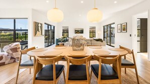 A modern dining area with a round table, wooden chairs, and pendant lighting. - Modern Wanaka Home | Mountain Views | Sleeps 6 (Wānaka)