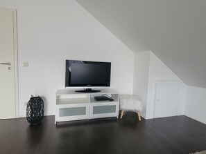A white entertainment unit with a flat-screen TV, a decorative basket, and a fluffy white stool. - Quiet Vacation Rental in the Countryside (Starzach)