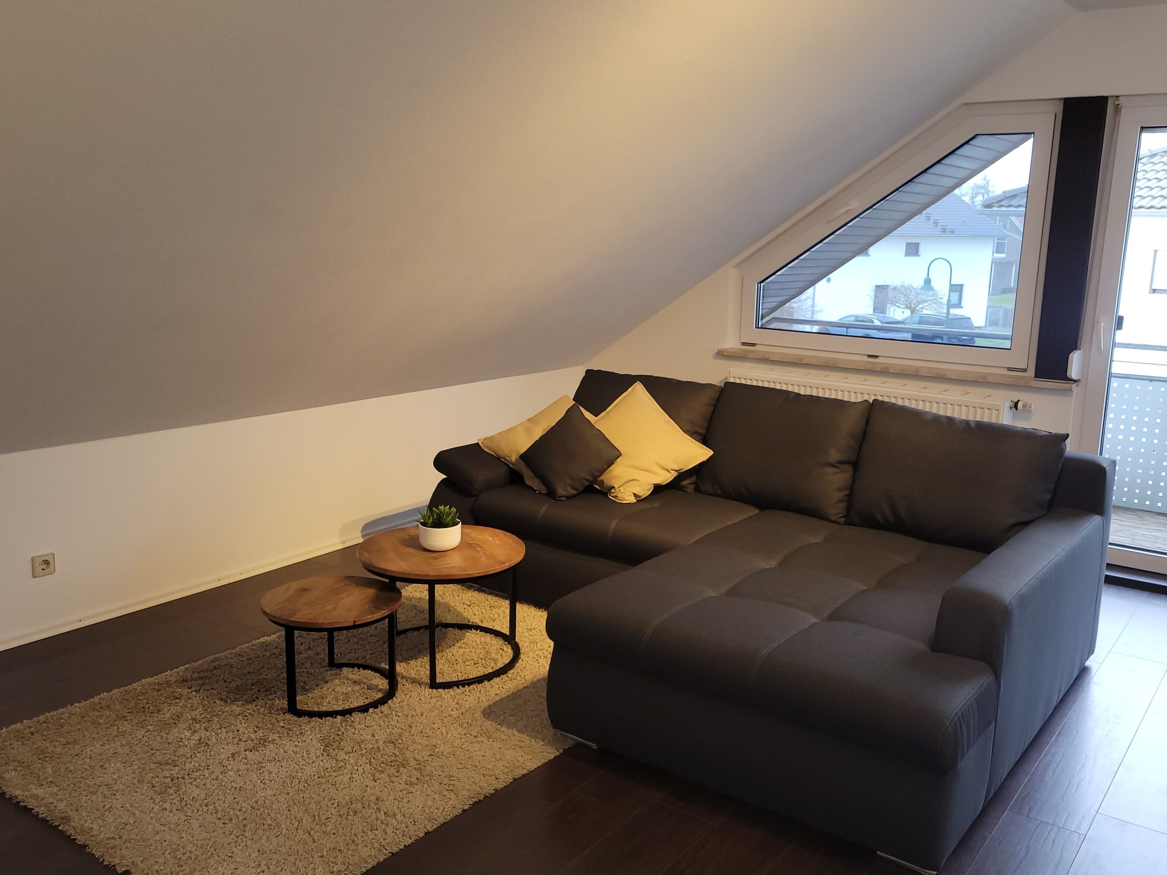 A modern living room with a dark grey sofa, a small round wooden table, and a potted plant.