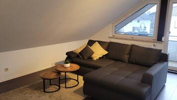 A modern living room with a dark grey sofa, a small round wooden table, and a potted plant.
