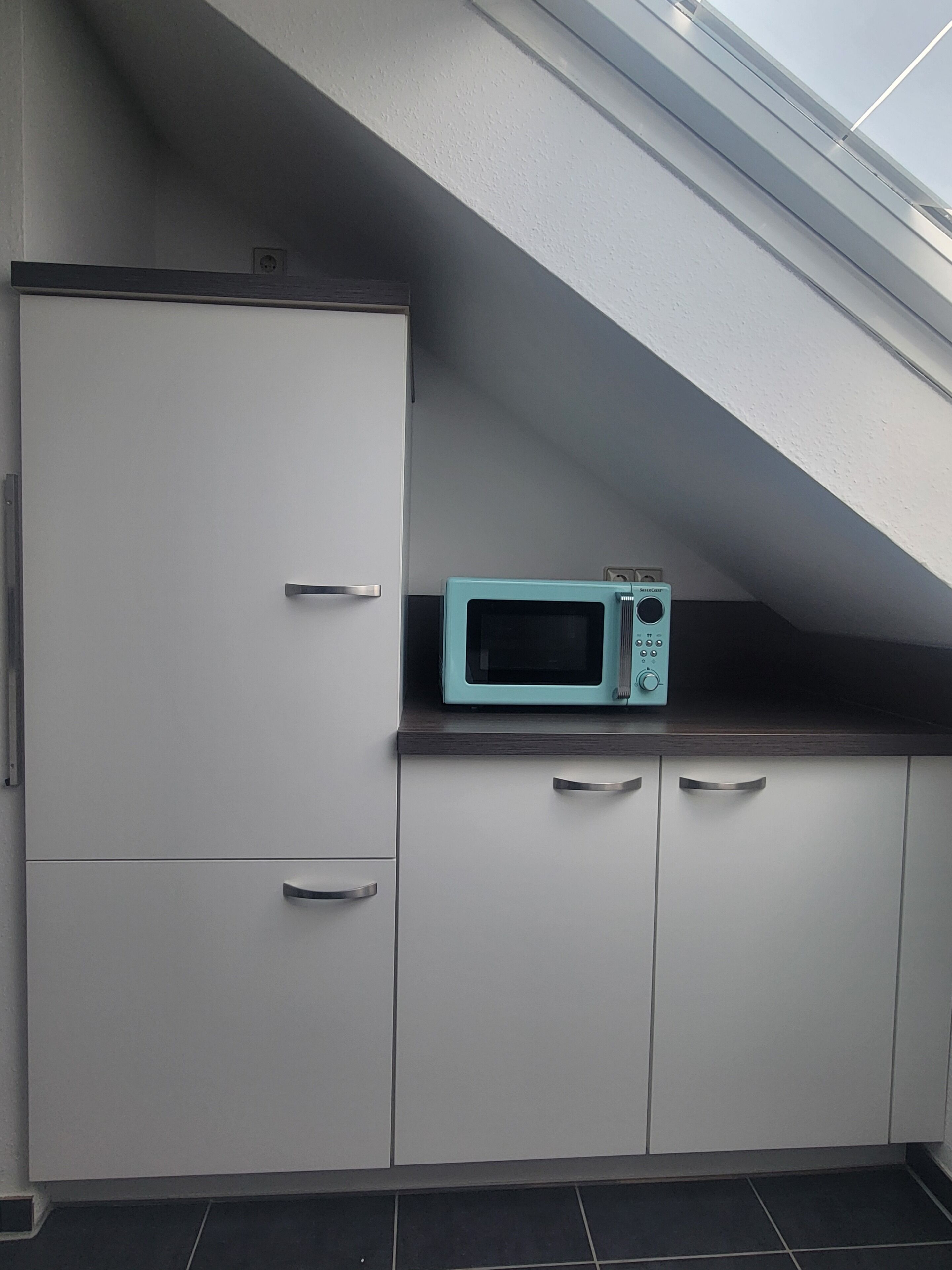 A kitchen with white cabinets, a teal microwave, and a skylight.