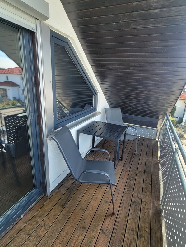 A balcony with a table and chairs, a window, and a dark wooden ceiling. - Quiet Vacation Rental in the Countryside (Starzach)