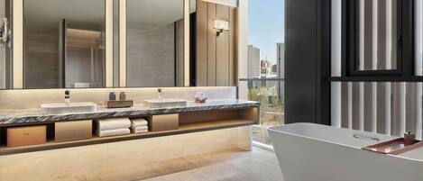 A modern bathroom with a large mirror, two sinks, a bathtub, and a view of the city.