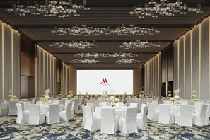 A large conference room with rows of tables and chairs, a large screen at the front, and a modern ceiling design.