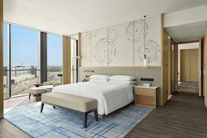A modern hotel room with a large bed, a desk, a chair, and a view of the city.