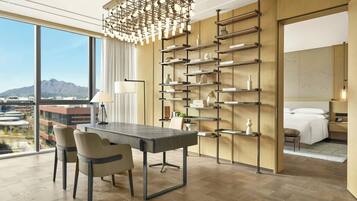 A modern hotel room with a dining area, a large window with a mountain view, and a decorative wall unit.