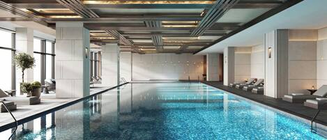 Une piscine intérieure moderne, avec une eau d’un bleu cristallin, entourée d’espaces de détente dotés de sièges.