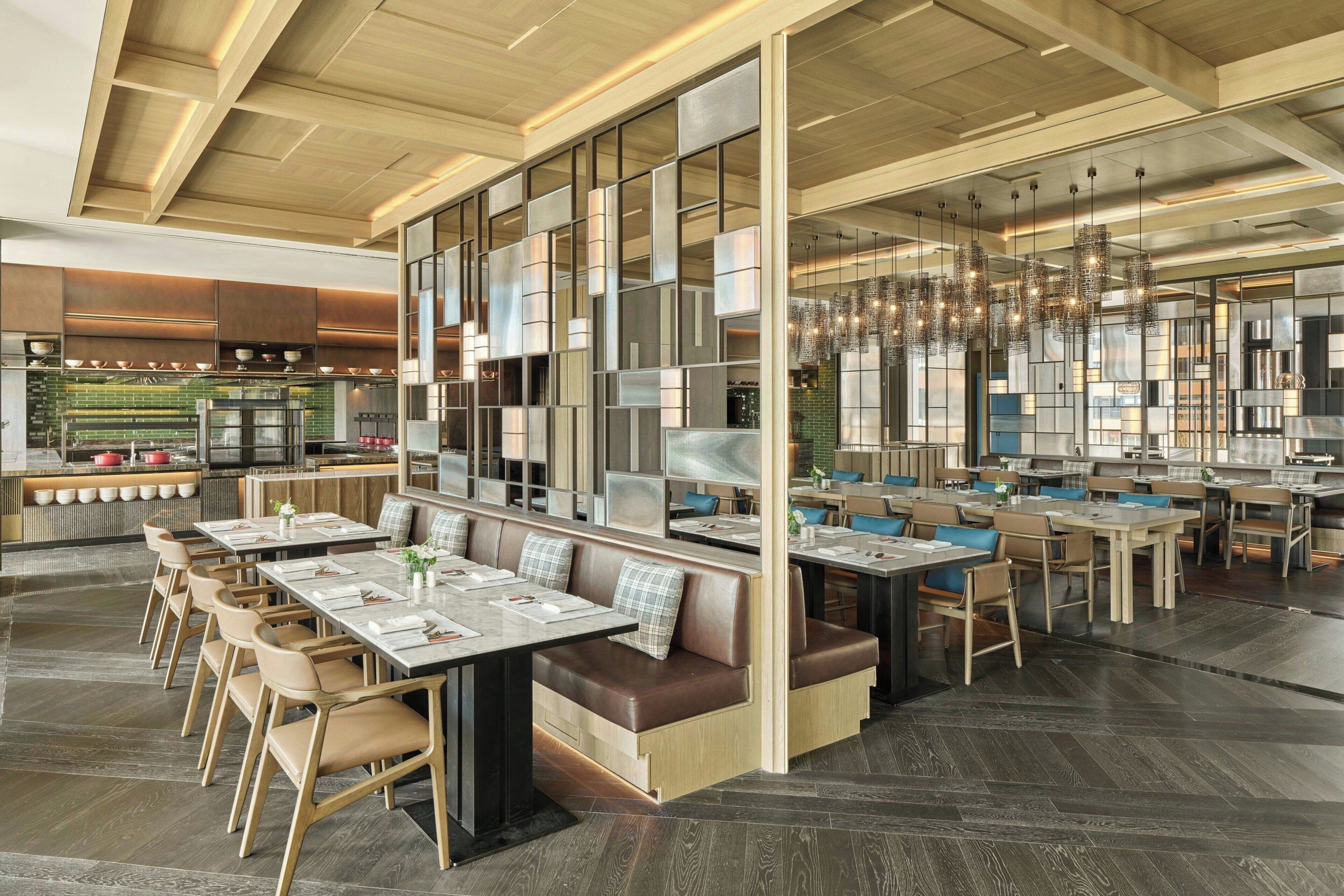 Ein modernes Restaurant mit hohen Decken, Holzvertäfelung und verschiedenen Sitzgelegenheiten, darunter Sitzecken und Tische.