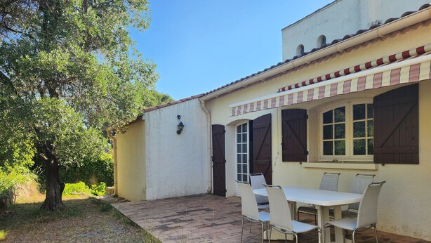 A patio with a table and chairs, a tree, and a building with a tiled roof and shutters. - Country House (Saint-Drézéry)