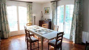 A dining area with a white table, wooden chairs, and a view of the outdoors through large windows. - Country House (Saint-Drézéry)