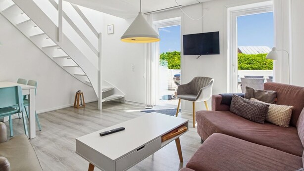 En moderne stue med trappe, fladskærms-tv og sofa med puder.
