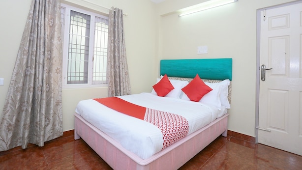 A bedroom with a bed, curtains, a window, a door, and a wall-mounted light fixture. - Classic Ambalathara Eastfort (Thiruvananthapuram)