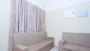 A living room with two sofas, a curtain, and a wall-mounted light switch. - Classic Ambalathara Eastfort (Thiruvananthapuram)