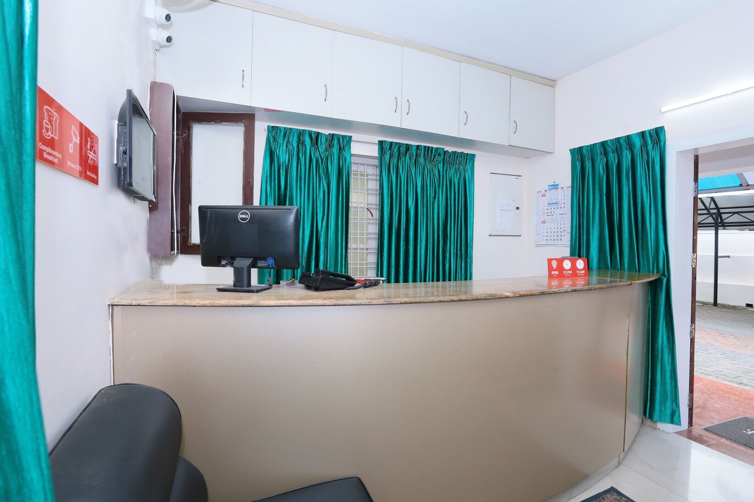 A reception area with a desk, computer, telephone, and green curtains.