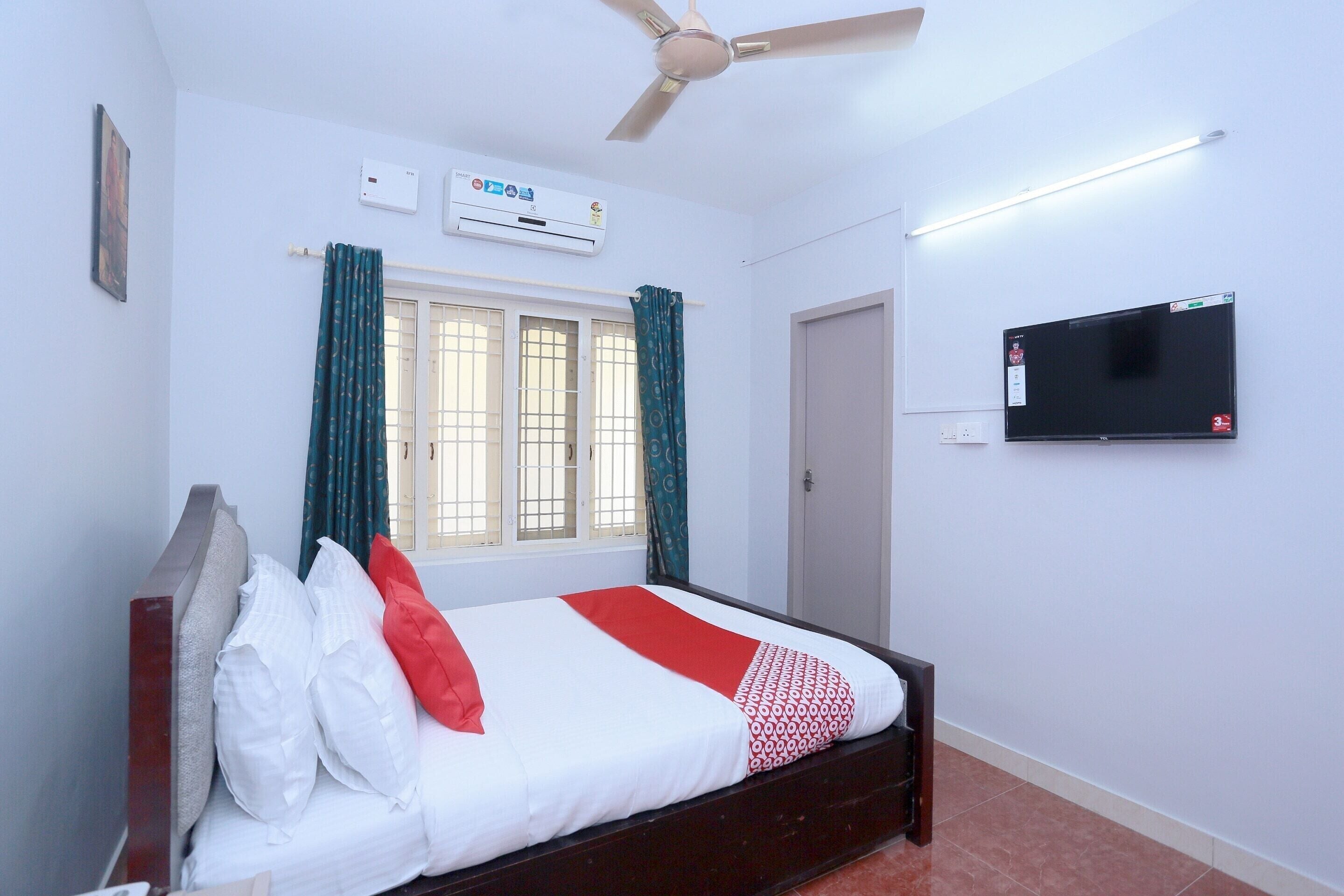 A bedroom with a bed, an air conditioner, a ceiling fan, a television, and a window with curtains.