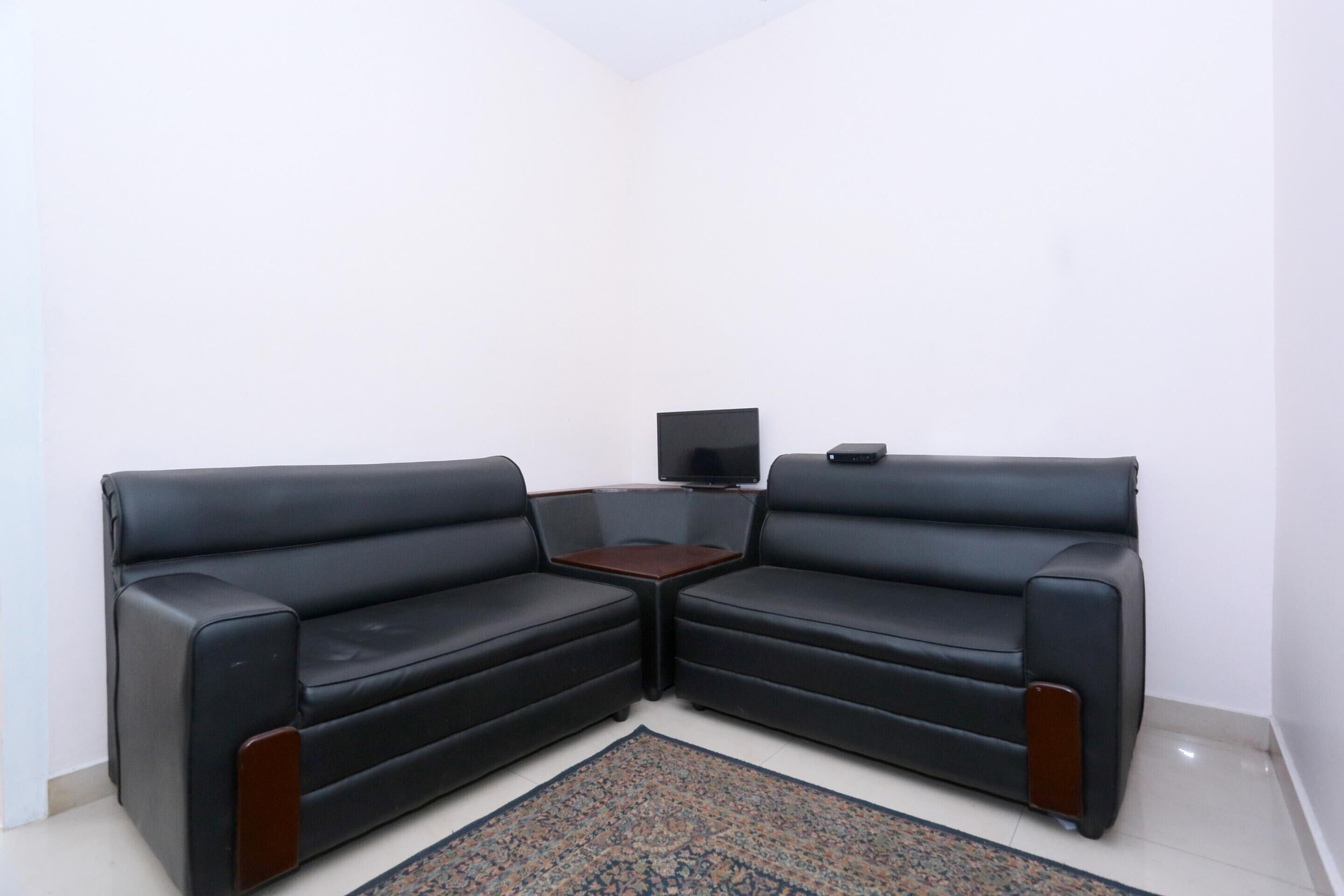 A corner living room with two black leather sofas, a small wooden coffee table, and a flat-screen TV mounted on the wall.