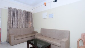 A living room with two sofas, a glass-top coffee table, a curtain, and a ceiling-mounted light fixture. - Classic Ambalathara Eastfort (Thiruvananthapuram)