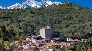 Un pueblo con una imponente torre de piedra, rodeado de edificios con techos de tejas rojas, con montañas nevadas al fondo.