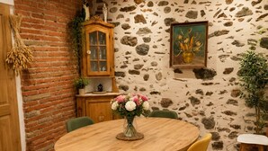 Un comedor rústico con una mesa redonda de madera, sillas amarillas, un aparador y una pared de piedra con un cuadro.