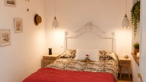 Un dormitorio con cama, un banco, una mesita de noche y una planta colgante.