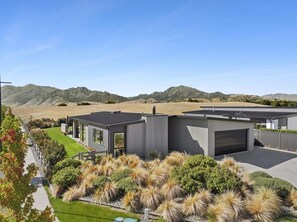 A modern two-story house with a garage, surrounded by landscaped gardens and a view of mountains.