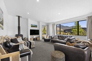 A modern living room with a fireplace, leather sofas, a flat-screen TV, and a large window offering a mountain view.