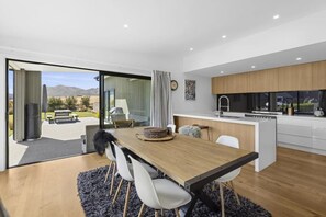 A modern kitchen with a central island, a dining area with a wooden table and chairs, and a sliding glass door leading to an outdoor patio.