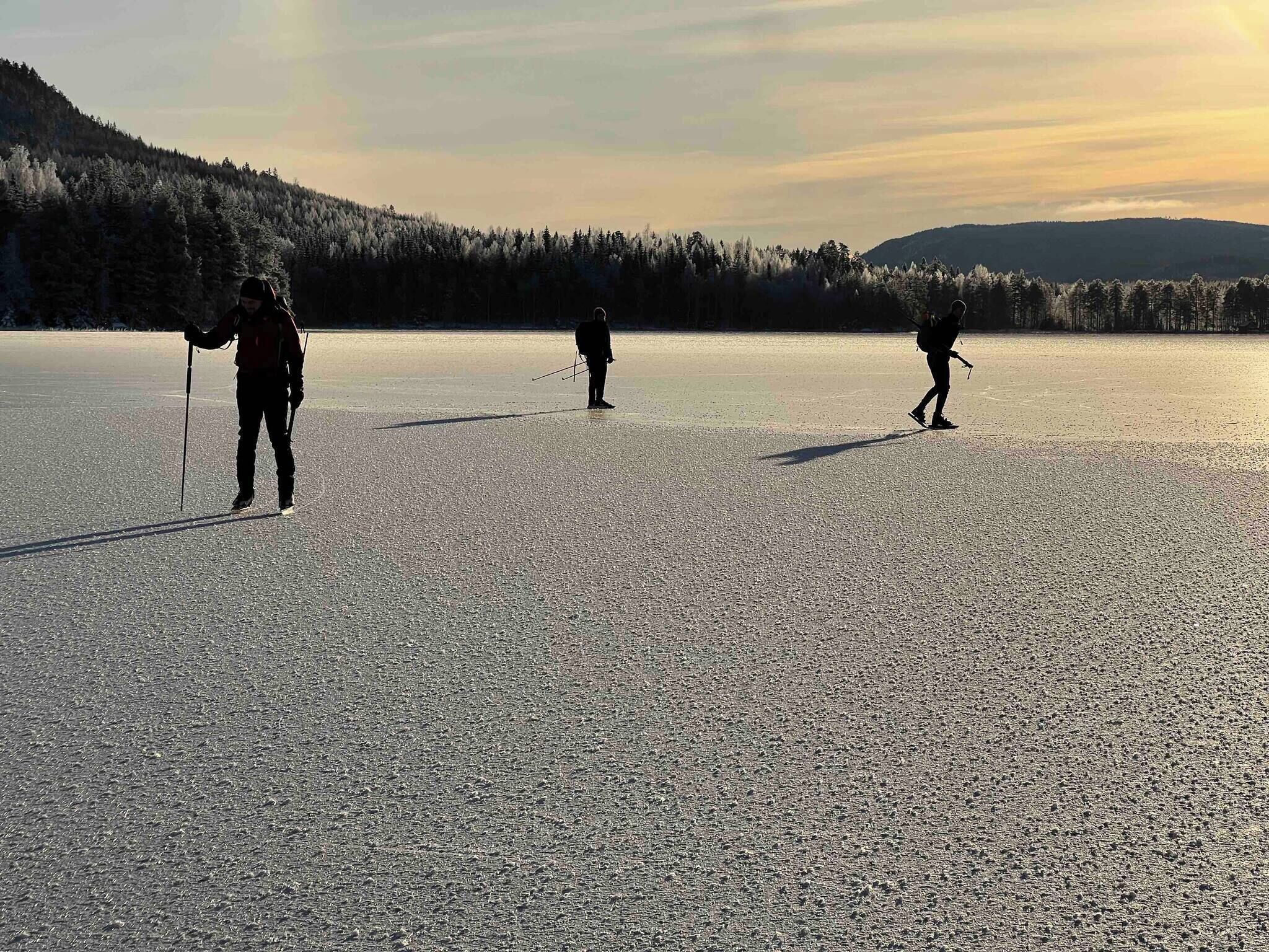 A flat, open landscape with three individuals cross-country skiing.
