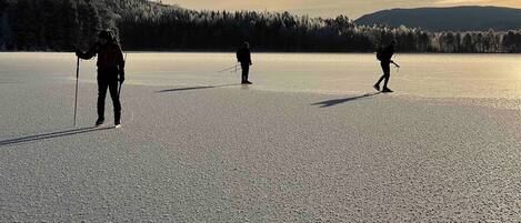 A flat, open landscape with three individuals cross-country skiing.