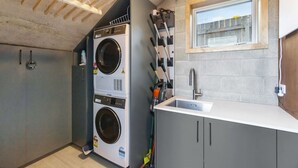 Een kleine wasruimte met twee gestapelde wasmachines, een klein raam en een wastafel.