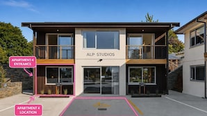 Een modern gebouw met de aanduiding 'ALP STUDIOS', een inrit en gemarkeerde parkeerplaatsen voor 'APARTMENT 4'.