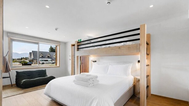 Een moderne slaapkamer met een stapelbed, een groot raam met uitzicht, een nachtkastje en een donkergroene bank.