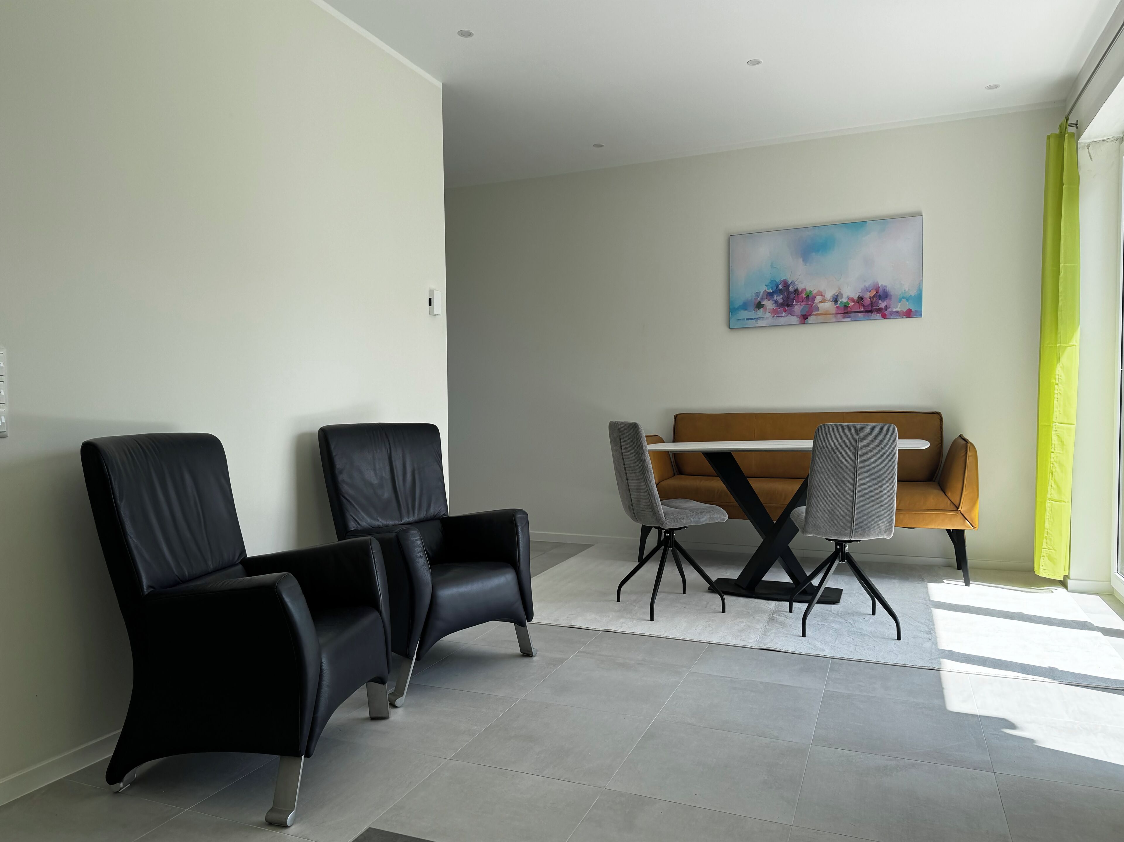 A modern room with a sofa, two black chairs, a table, and a painting on the wall.
