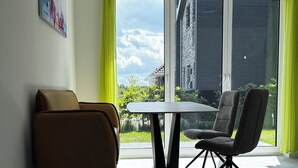 Una sala de estar moderna con un sofá, una mesa de comedor y sillas, ventanas amplias con cortinas y un cuadro en la pared.