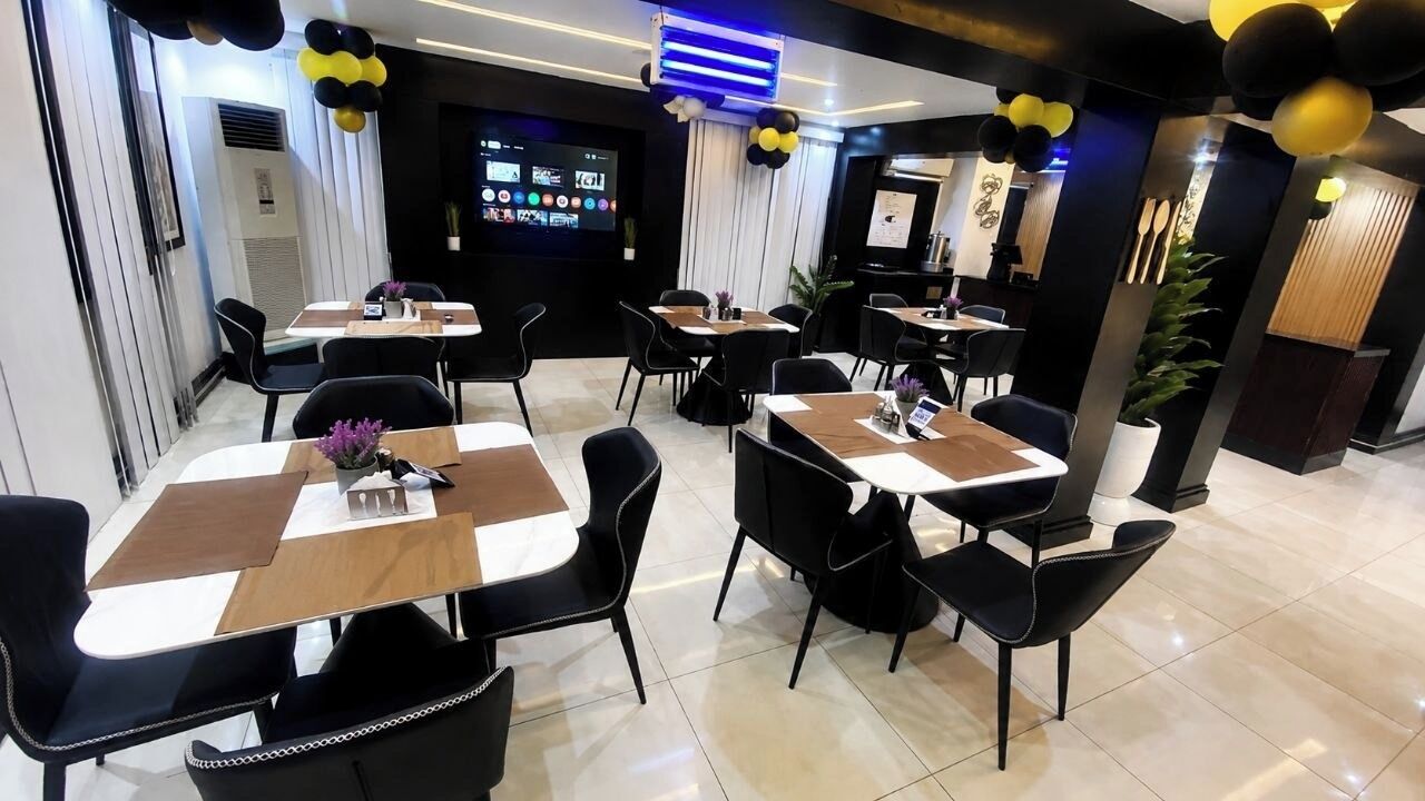 Eine moderne Hotelhalle mit mehreren Tischen und Stühlen, einem großen digitalen Bildschirm und dekorativen Ballons.
