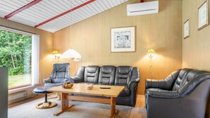 Ein modernes Wohnzimmer mit Ledersofas, einem Holztisch und einem großen Fenster mit Blick auf Grünflächen.