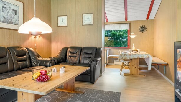 Ein modernes Wohnzimmer mit einer Couch, einem Holztisch mit Obst, einem Essbereich mit Tisch und Stühlen und Blick auf Grünflächen draußen.