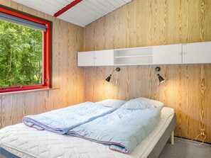 Een slaapkamer met een bed, een raam met rode omlijsting, houten wandbekleding en een wit hoofdeinde met planken.
