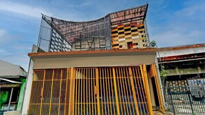 A building with a gated entrance, a sloped roof, and a visible staircase leading to the upper level. - Cozy Double Escape W/ Free Wifi and Parking (Surabaya)