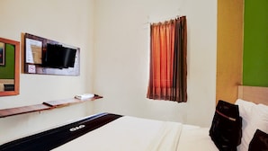 A hotel room with a bed, a TV mounted on the wall, a window with curtains, and a wooden shelf with a remote control. - Cozy Double Escape W/ Free Wifi and Parking (Surabaya)