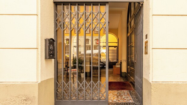 Entrada de hotel com portão de metal, balcão de recepção e piso de azulejos.